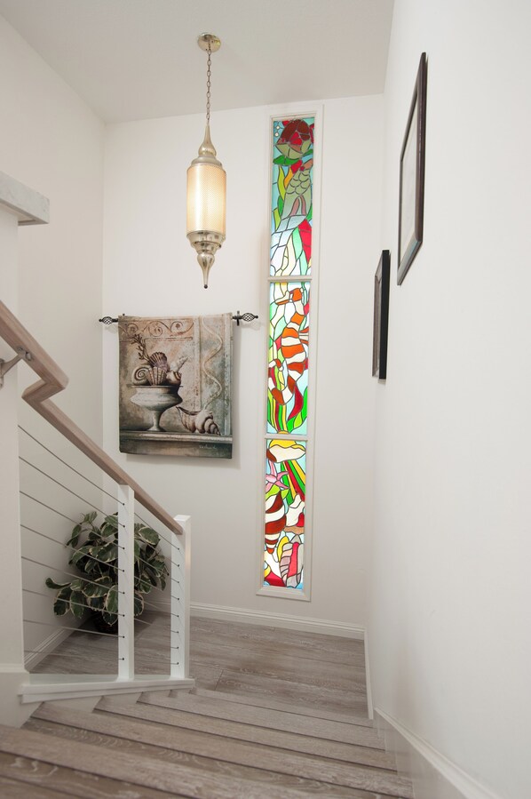 Una escalera con barandilla de madera, un colgador de luz y un vitral.