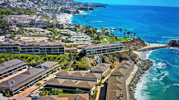 Una zona residencial costera con casas y edificios a lo largo de la orilla, que presenta una playa rocosa y aguas azul cristalino.