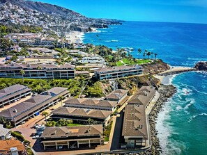 Una zona residencial costera con casas y edificios a lo largo de la orilla, que presenta una playa rocosa y aguas azul cristalino.