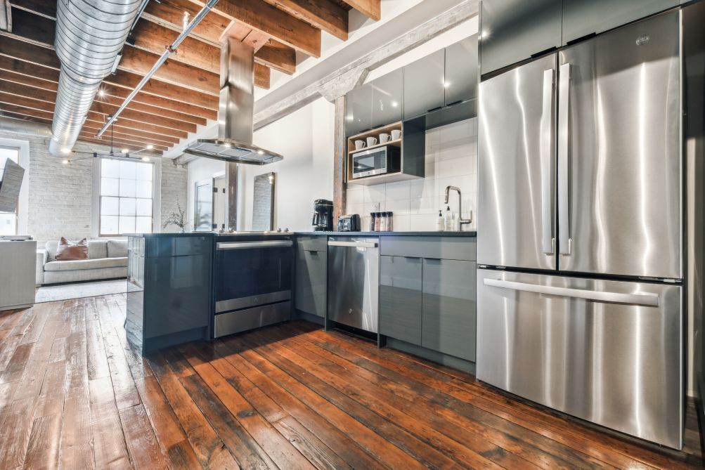 A modern kitchen with stainless steel appliances, wooden flooring, and a loft-style ceiling.