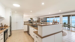 Una cocina moderna con una isla central, lavavajillas y vista al océano a través de amplios ventanales.