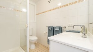 Kylpyhuone, jossa on wc, suihku ja peilillä varustettu pesuallas.