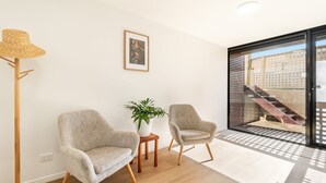 Ein modernes Wohnzimmer mit zwei Sesseln, einer Stehlampe, einer Topfpflanze und einem gerahmten Bild an der Wand.