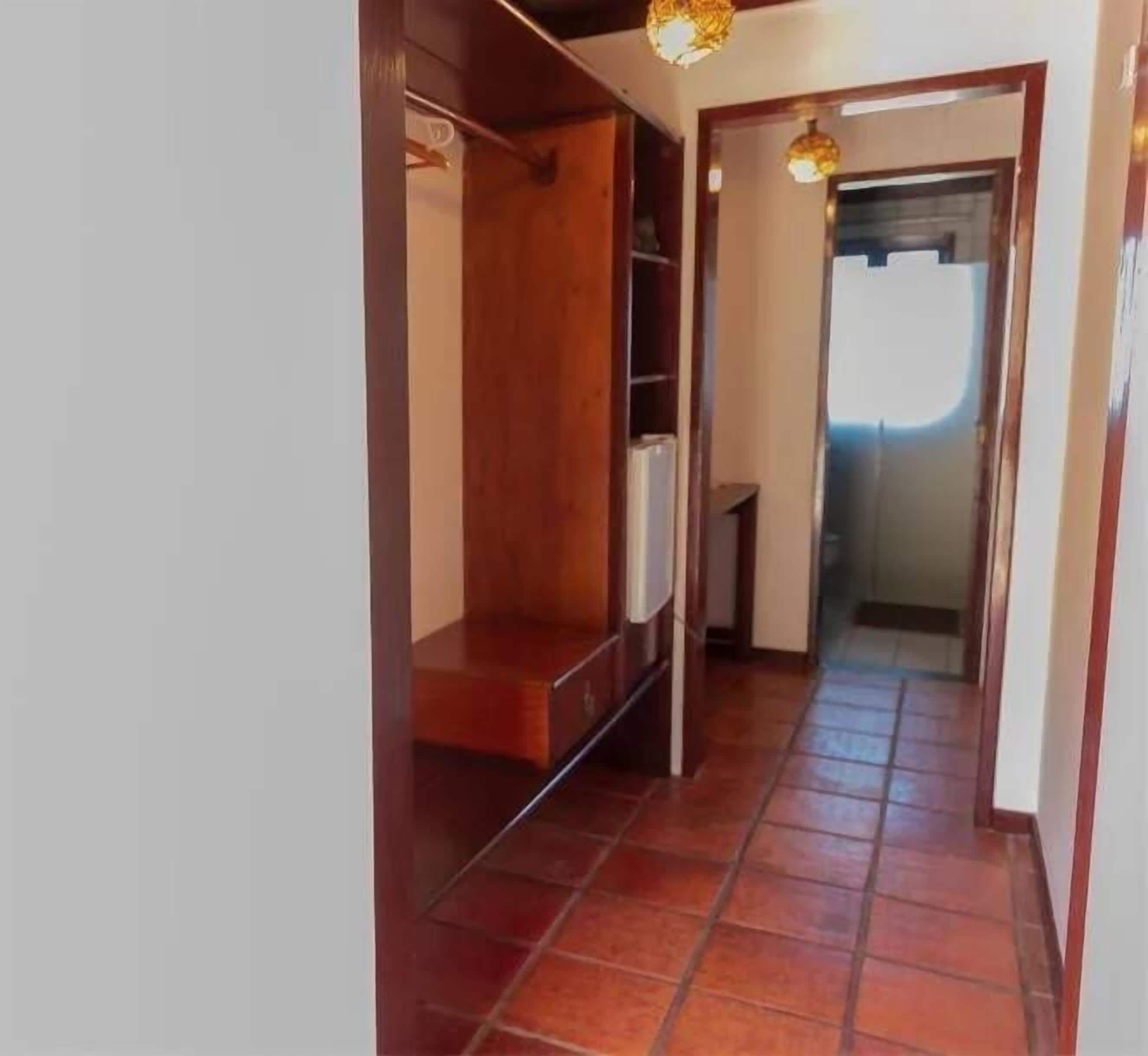 A narrow hallway with a wooden bench, tiled flooring, and a door leading to another room.