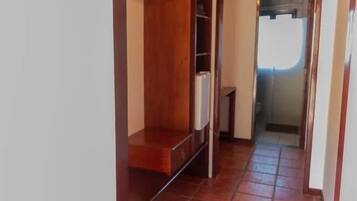 A narrow hallway with a wooden bench, tiled flooring, and a door leading to another room.