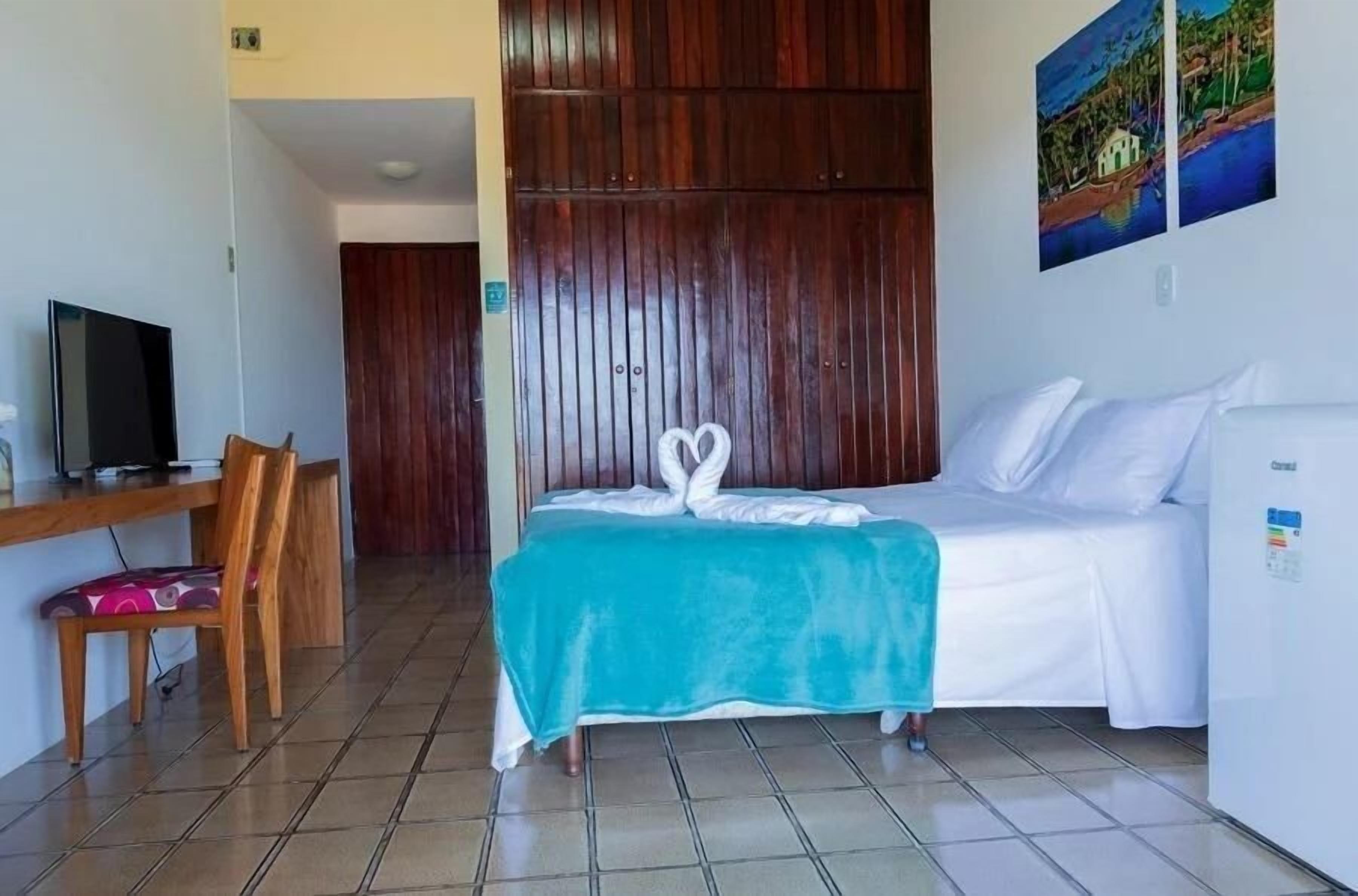A hotel room with a bed, a desk with a chair, a television, and a painting on the wall.