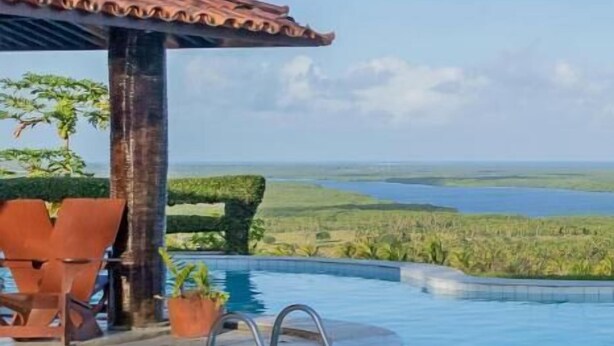 Un espace piscine offrant une vue sur un paysage naturel, un coin salon abrité et un escalier pour accéder à la piscine.