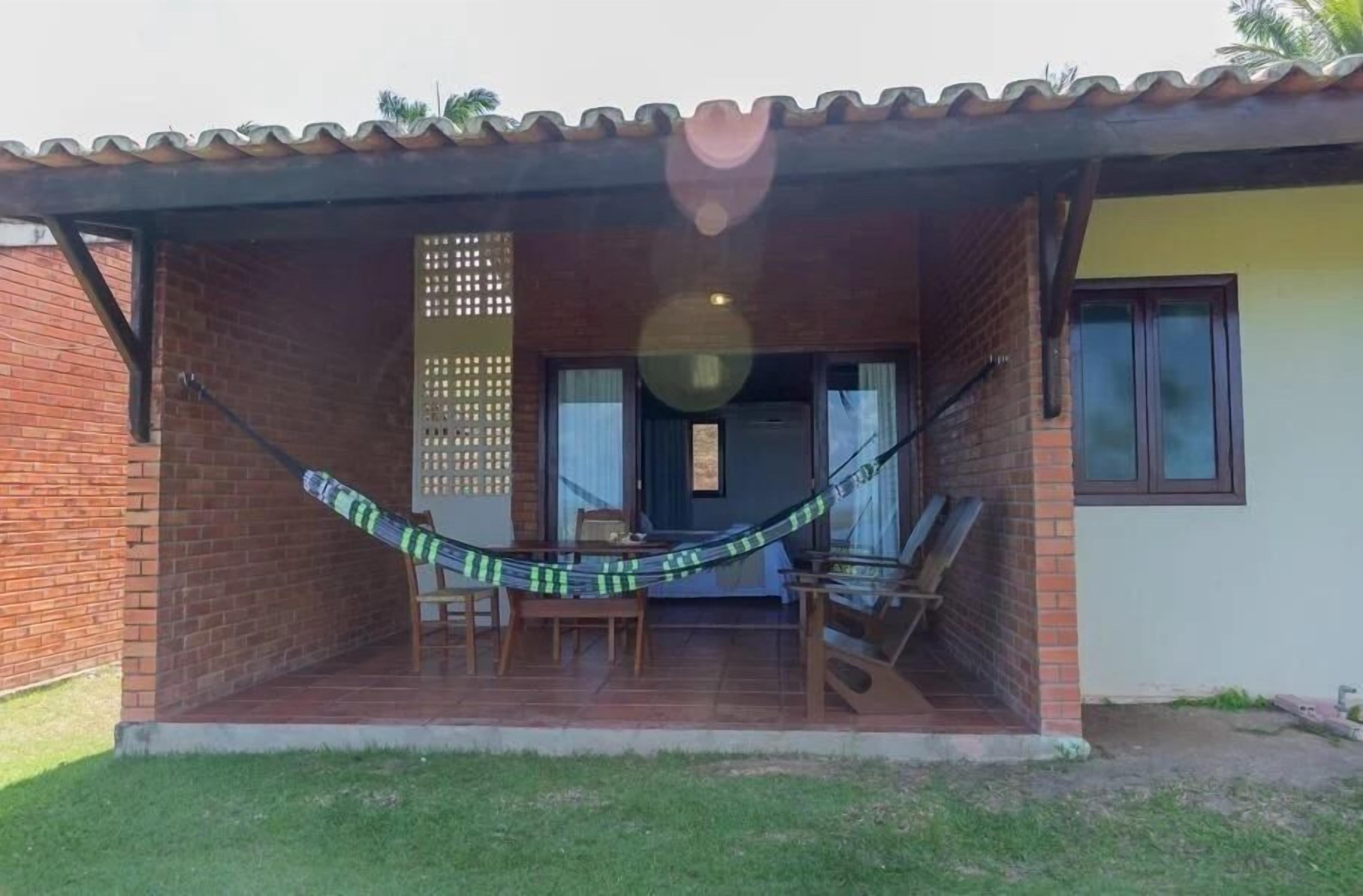 A covered patio with a hammock, a wooden table, and chairs.