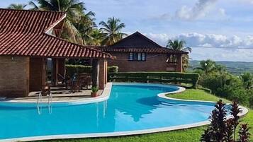 A large outdoor swimming pool with a curved design, surrounded by a well-maintained lawn and palm trees.