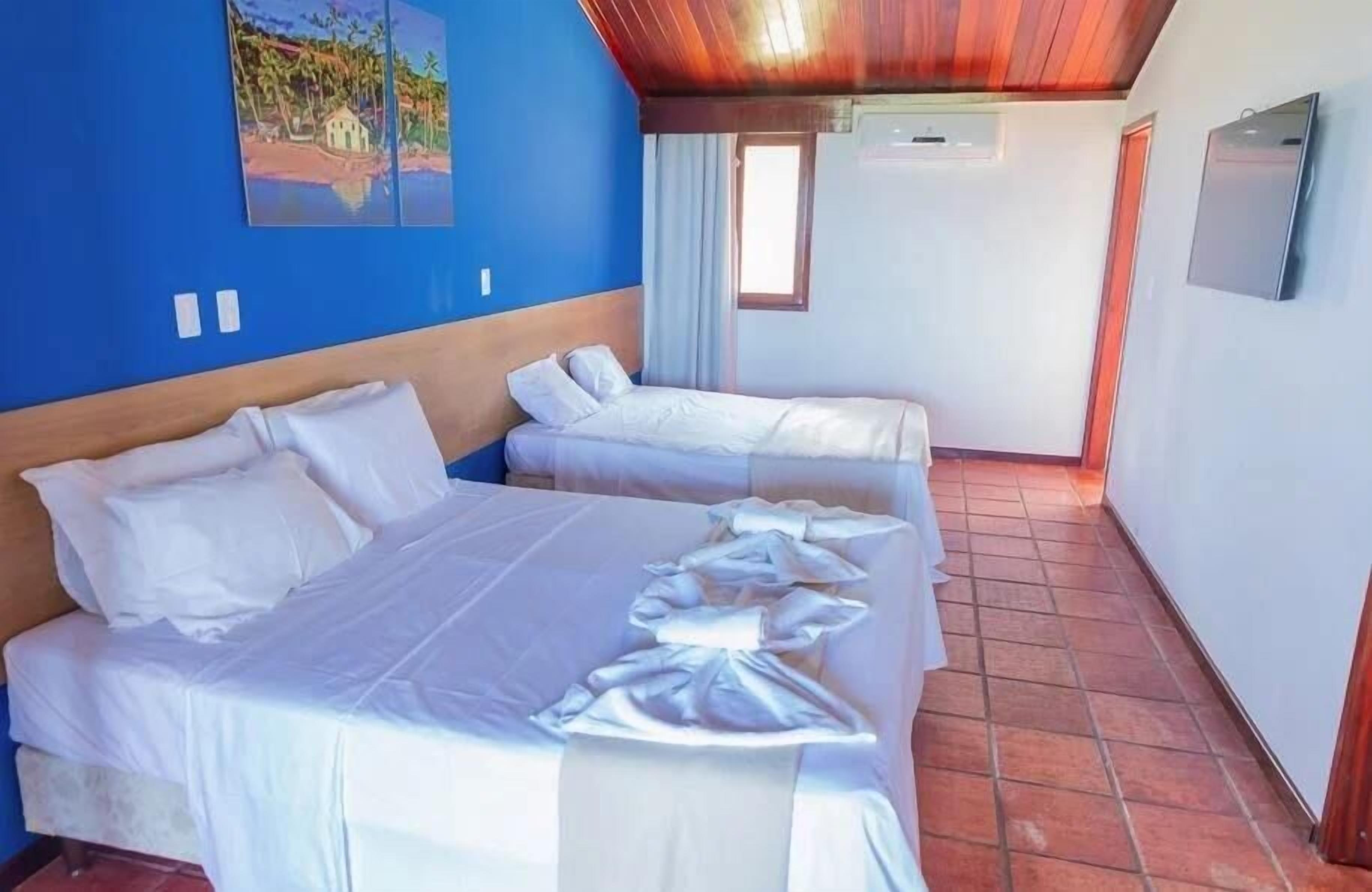 A room with two beds, a painting on the wall, a window, and a TV mounted on the wall.