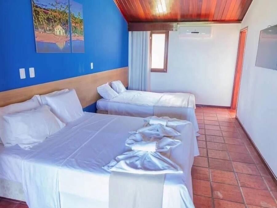 A room with two beds, a painting on the wall, a window, and a TV mounted on the wall.