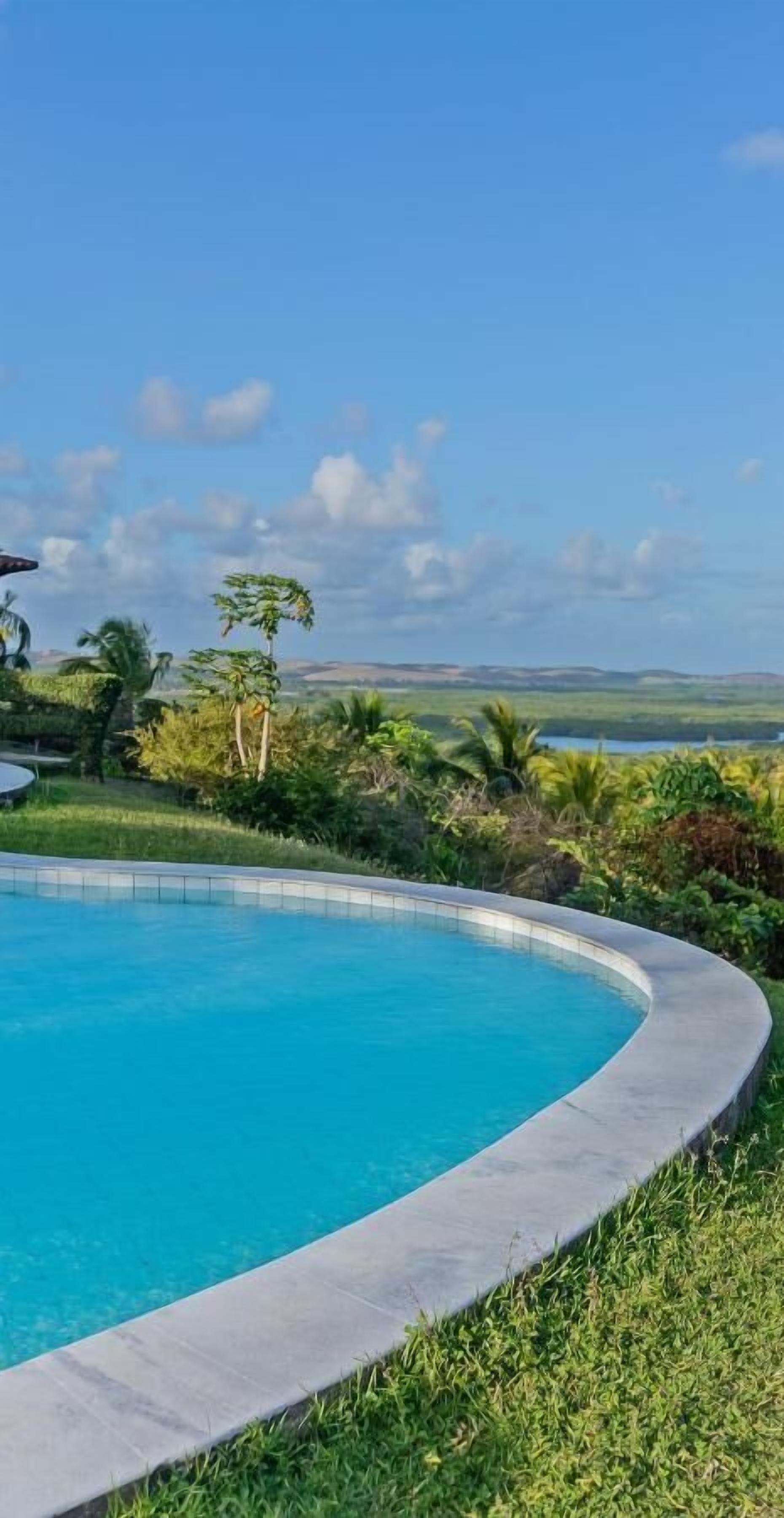 A swimming pool with a curved edge, surrounded by lush greenery and a view of distant hills.
