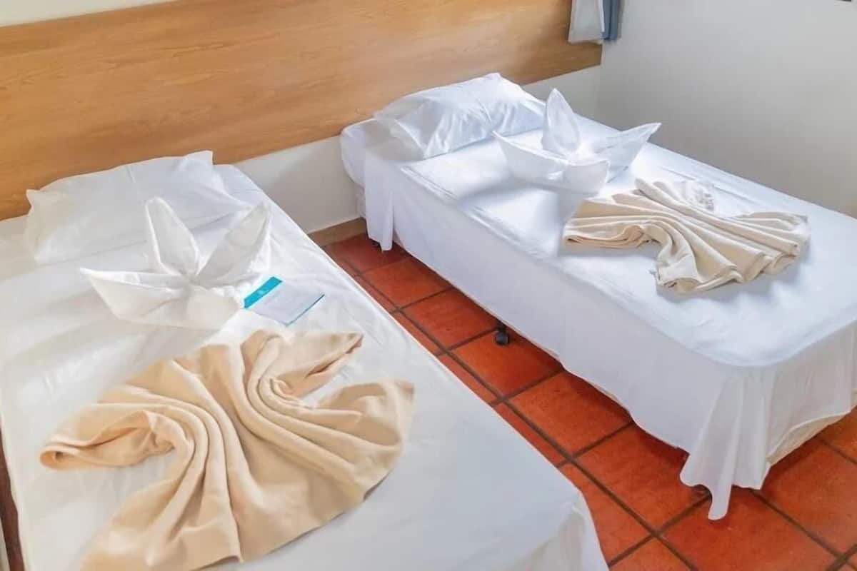 Une chambre d’hôtel avec deux lits, chacun recouvert de draps blancs et de serviettes beiges disposées de manière décorative.