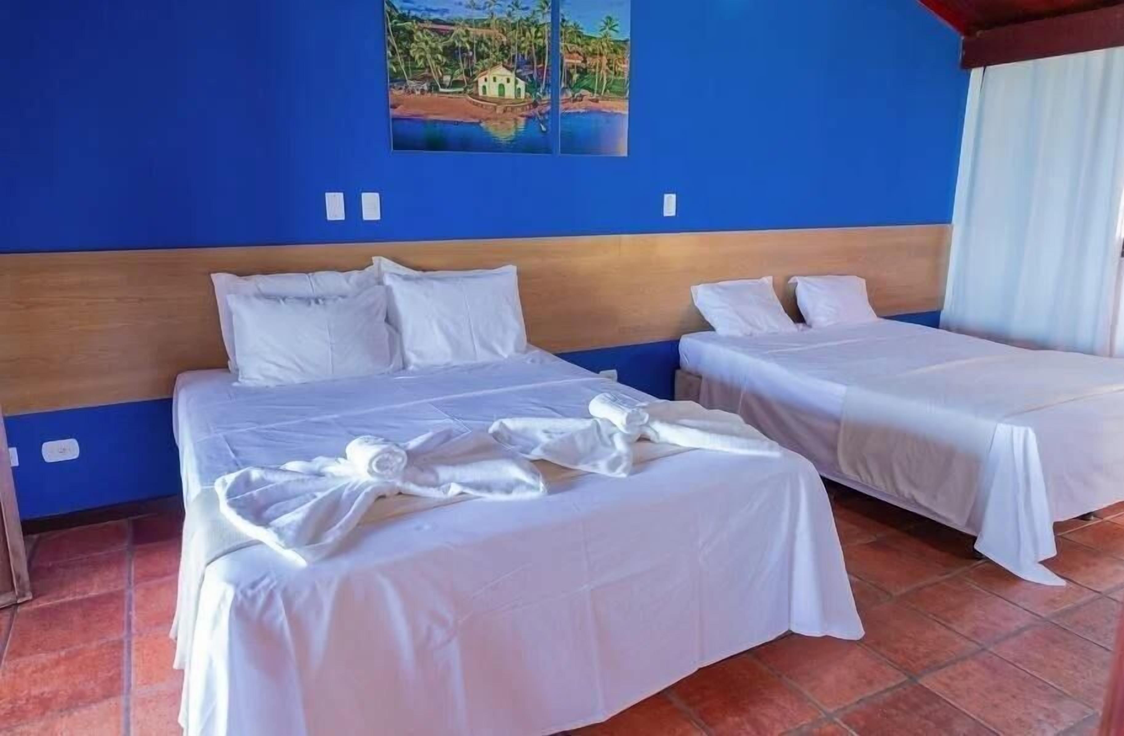 Habitación de hotel con dos camas, un cabecero de madera y un cuadro de una escena tropical en la pared.