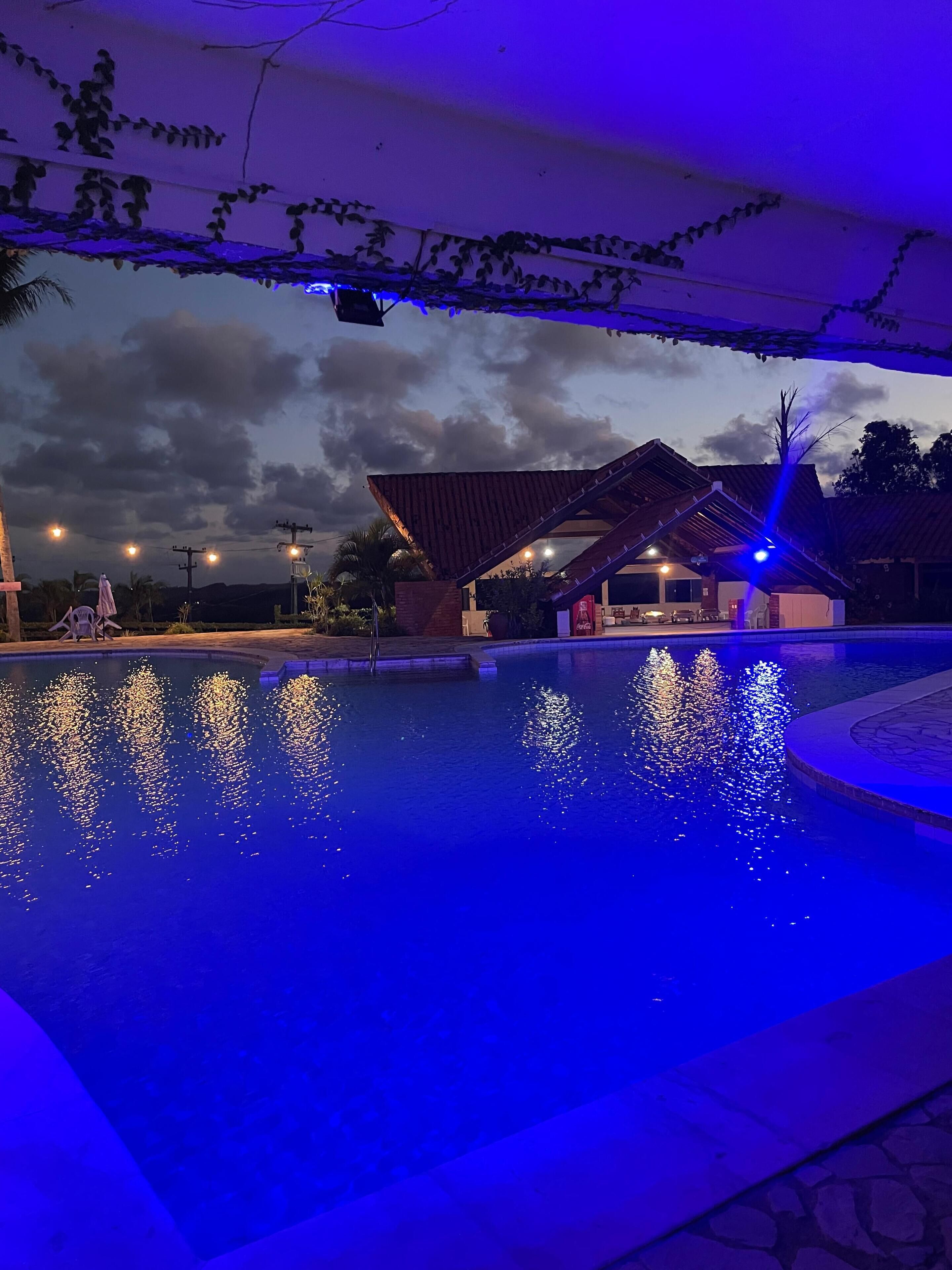 En swimmingpool med vandleg, et overdækket område med tag, og en bygning i baggrunden.