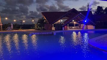 En swimmingpool med vandleg, et overdækket område med tag, og en bygning i baggrunden.