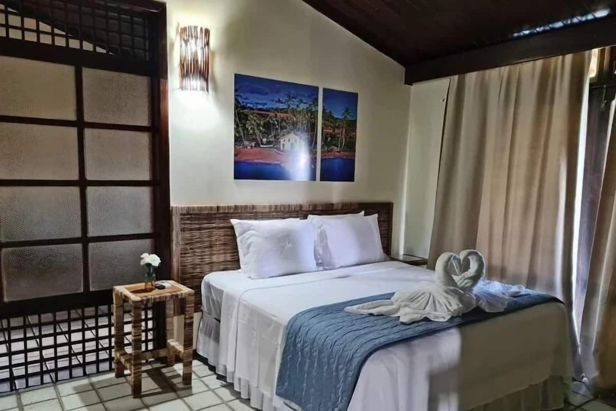 Une chambre d’hôtel avec un lit, une petite table sur laquelle est posé un vase, et deux tableaux accrochés au mur.