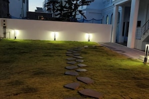 A pathway with stepping stones leading to a building entrance, surrounded by grass and illuminated by wall-mounted lights. - Daytime (Penghu)