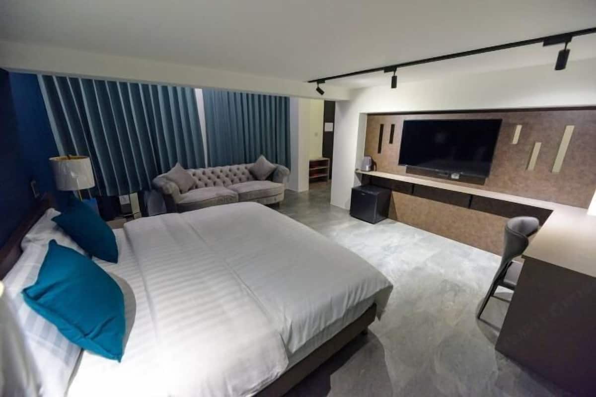 A modern hotel room with a large bed, a sofa, a TV, and a minibar.
