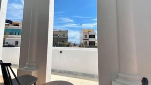 A balcony with white columns, a black chair, and a view of buildings under a clear sky. - Daytime (Penghu)