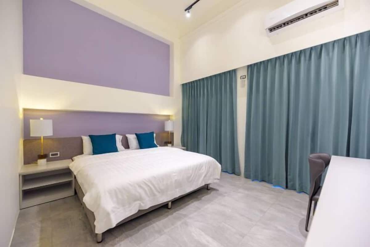 A hotel room with a bed, nightstands, a desk, and a window with curtains.
