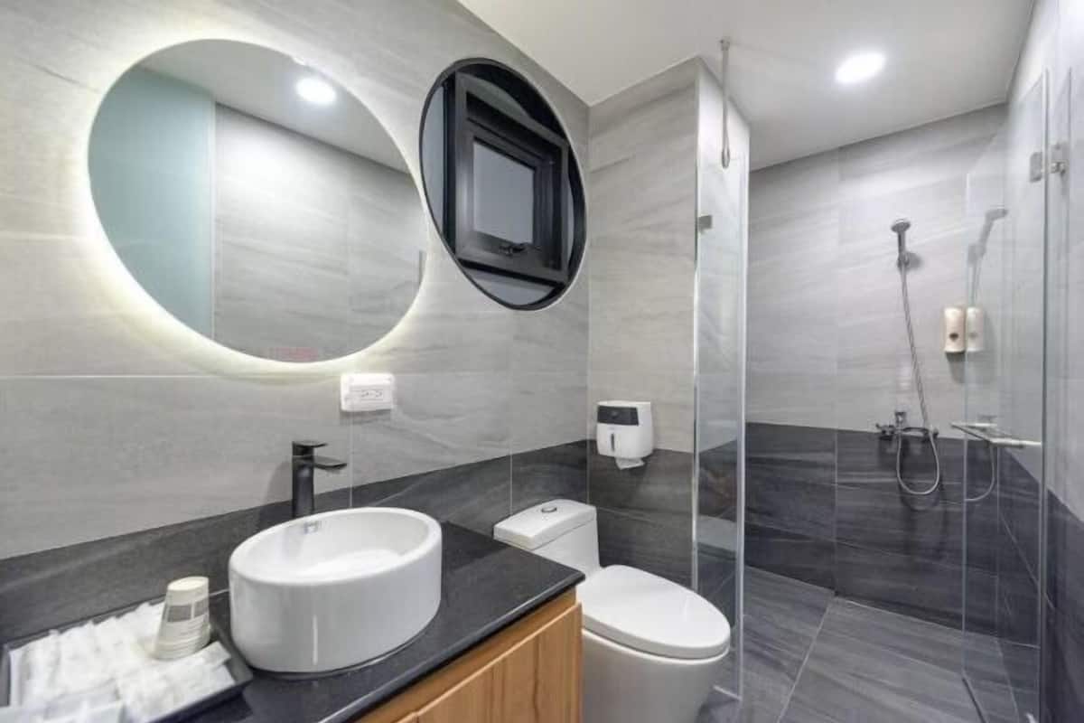 A modern bathroom with a round mirror, two sinks, a toilet, and a glass-enclosed shower.