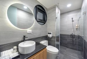 Une salle de bain moderne avec un grand miroir rond, deux vasques, des toilettes et une douche à l’italienne.