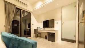 A modern hotel room with a blue sofa, a flat-screen TV, a desk, and a sliding door. - Daytime (Penghu)