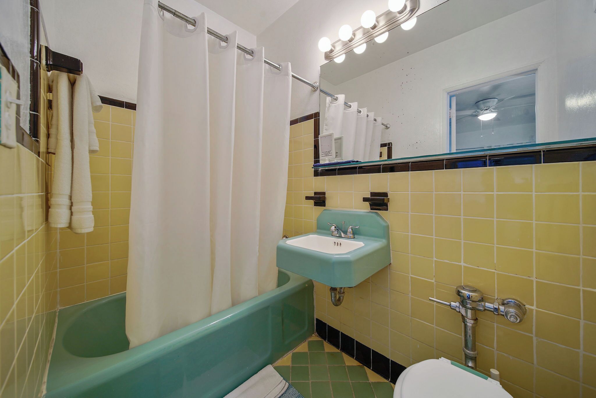 A bathroom with a green bathtub, a white sink, and a mirror with lights above it.