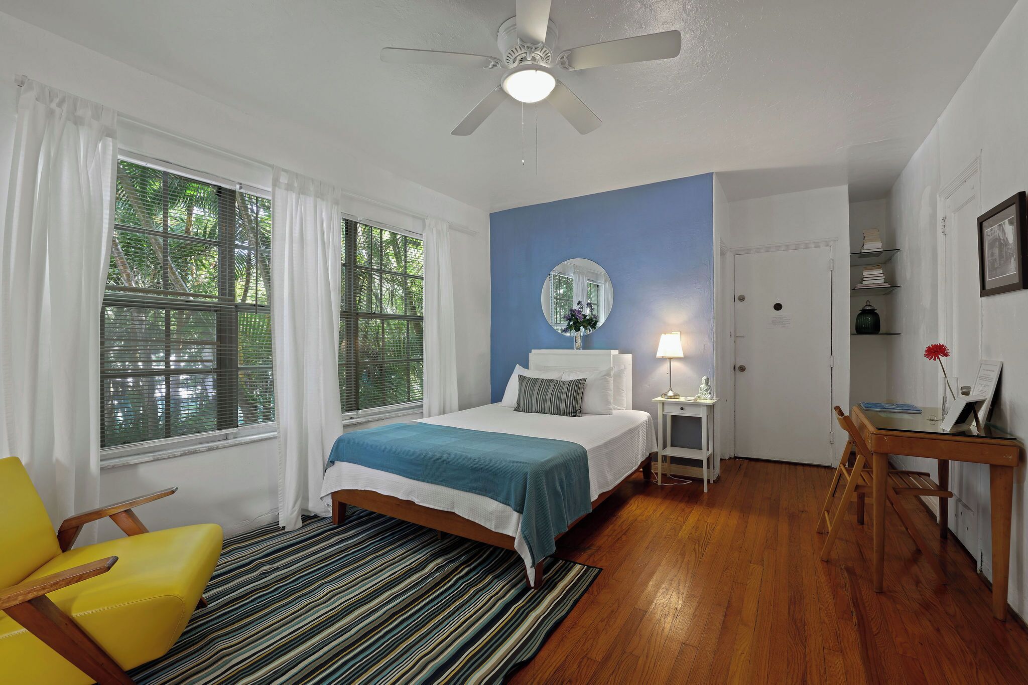 Ein Schlafzimmer mit Bett, Stuhl, Schreibtisch und Deckenventilator.