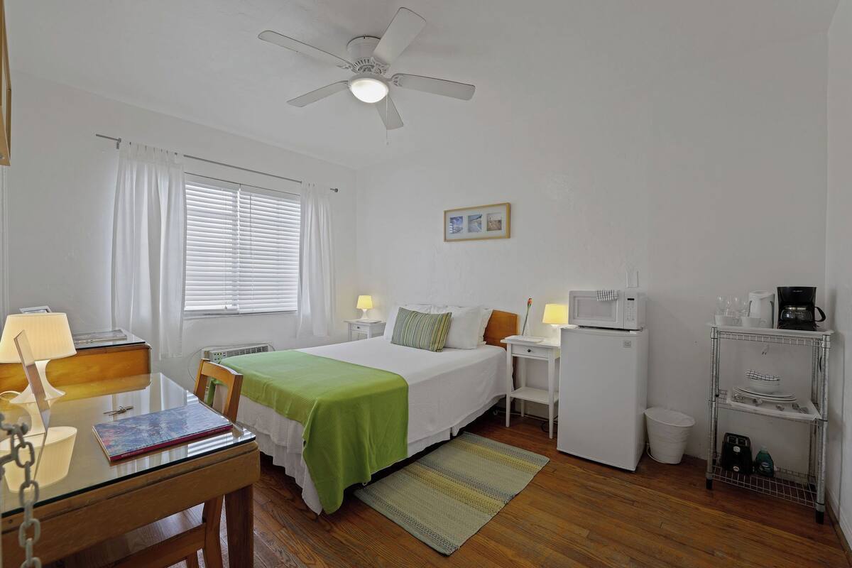 Een schone, goed verlichte kamer met een bed, nachtkastjes, een bureau, een stoel, een magnetron en een kleine kitchenette.