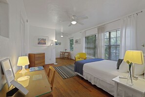 A hotel room with a bed, a desk, a chair, a ceiling fan, and a window with blinds. - Barcelona Studios Guesthouse (Miami Beach)