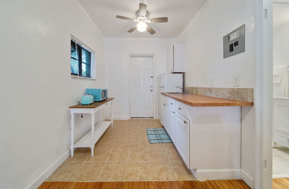 A small, clean kitchen with white cabinets, a wooden countertop, and a ceiling fan.