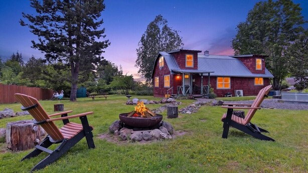 Une maison avec un foyer extérieur, deux fauteuils Adirondack et une terrasse en bois.
