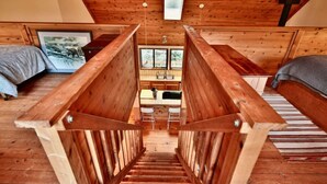 Una cabaña de madera con una escalera central que conduce a una zona de cocina, dos camas a cada lado y un ventanal con vistas panorámicas.