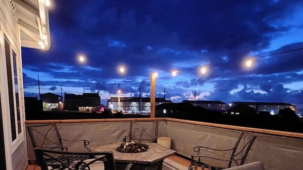 A rooftop patio with outdoor furniture, a fire pit, and a view of the city skyline at dusk. - L`escapade -The Getaway (Lincoln City)