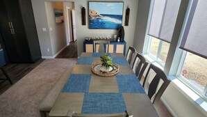A dining area with a long table, chairs, a central decorative piece, and a large window with a view. - L`escapade -The Getaway (Lincoln City)
