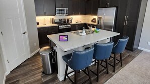 A modern kitchen with dark cabinets, stainless steel appliances, and a central island with bar stools. - L`escapade -The Getaway (Lincoln City)