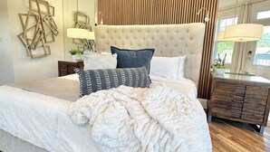 Ein modernes Schlafzimmer mit einer gesteppten Kopfteile, einem großen Spiegel und Holzboden.