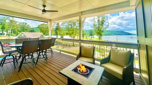 Ein überdachter Außenbereich mit Tisch und Stühlen, einem Feuerkorb und Blick auf einen See und Berge.
