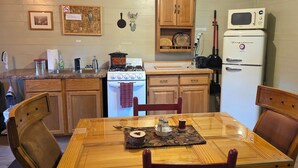 Una cucina compatta con mobili in legno, un fornello a gas, un forno a microonde e un frigorifero. C'è un tavolo da pranzo con sedie e un sottotavolo.