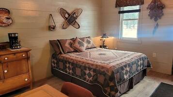 A cozy bedroom with a wooden bed, a dresser, a coffee maker, and a window with a view of trees.