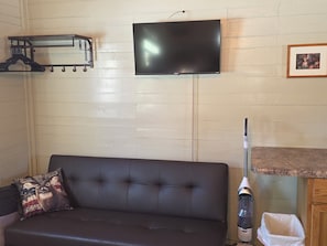 A room with a black leather sofa, a mounted flat-screen TV, a coat rack, and a framed picture on the wall.