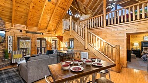 A cozy log cabin with a dining area, a staircase, and a living room with a sofa and a TV. - Incredible Vibes, Cozy Fires, and Pure Relaxation! (Sevierville)