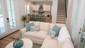 A spacious living room with a beige sofa, a coffee table, and a staircase leading to the kitchen. - 30A Fun in the Sun 5 minute walk to a Public Beach no Private Beach Hassles (Santa Rosa Beach)