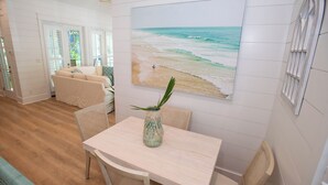 A dining area with a table and chairs, a vase with a plant, and a beach scene painting on the wall. - 30A Fun in the Sun 5 minute walk to a Public Beach no Private Beach Hassles (Santa Rosa Beach)