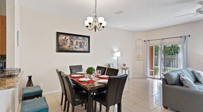 Uma sala de jantar com uma mesa posta para quatro pessoas, um candelabro e um quadro na parede.