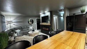 A modern living room with a wooden dining table, a grey sofa, and a TV mounted on the wall. - Oasis in The City - Executive Retreat- Long Term Welcome (Grand Junction)