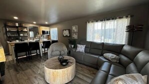 A living room with a sofa, ottoman, and dining area with chairs and a table. - Oasis in The City - Executive Retreat- Long Term Welcome (Grand Junction)