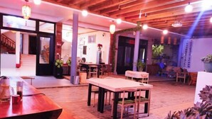 A spacious indoor area with wooden flooring, multiple tables and chairs, and a staircase leading to an upper level.